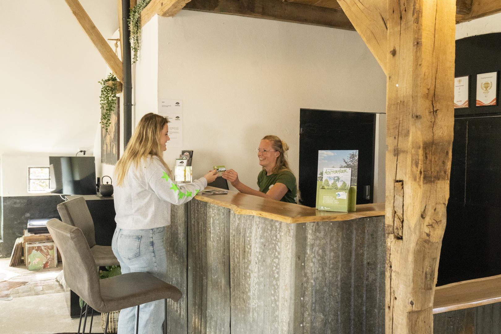Bij de receptie van een camping overhandigd de receptioniste een kaartje aan een gast.