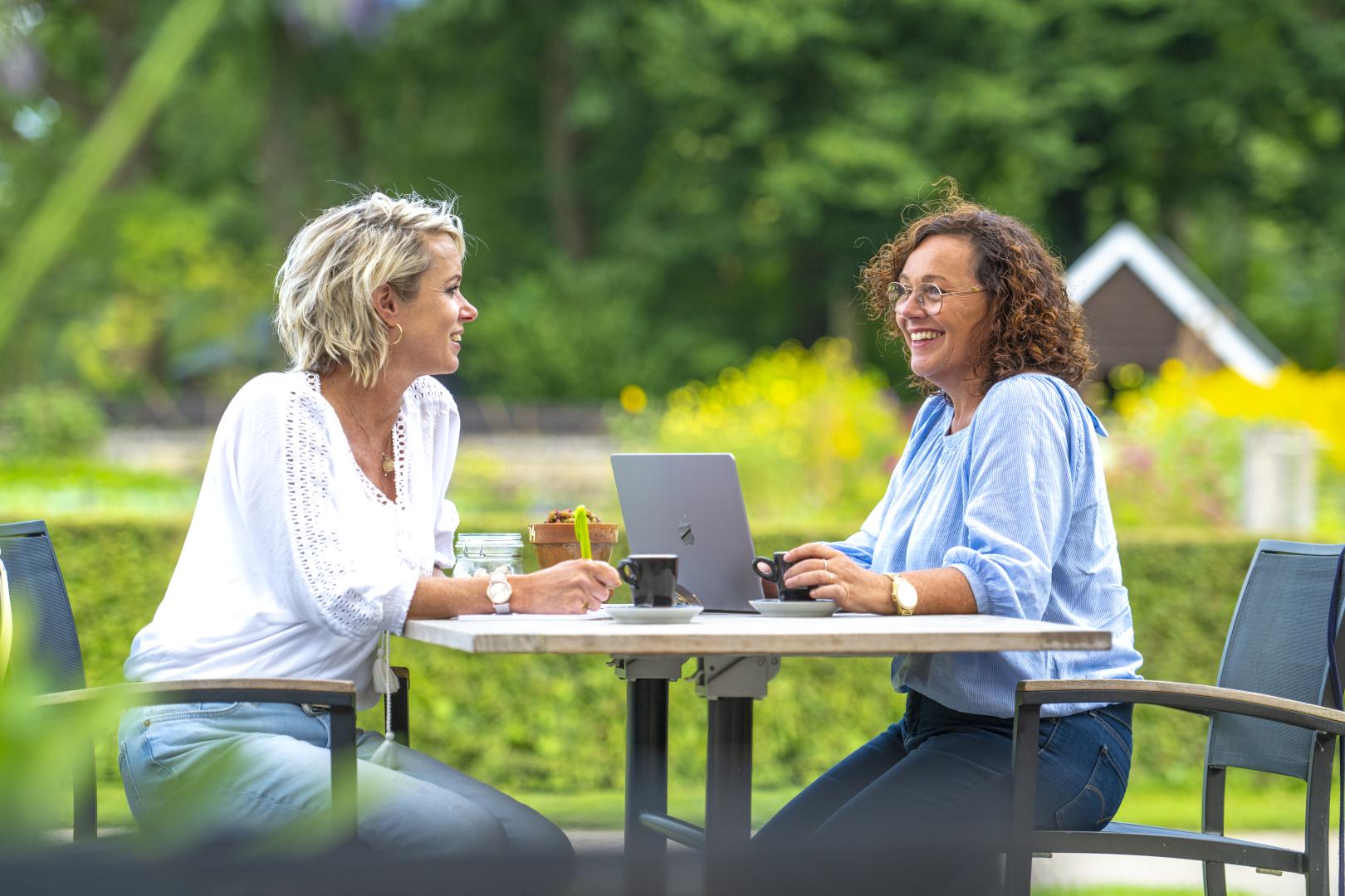 Recreatieondernemer in gesprek met een adviseur tijdens een persoonlijk adviesgesprek op een terras in een groene omgeving.